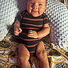 baby, infant, smile, striped_clothing, onesie, pillow, patterned_blanket, tiger_design, golden_chains, sitting, cute, happy, indoor, young_child, face, legs, hands, black_socks, texture, soft