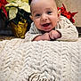 Omar is registered to the contest to win money with this photo: baby, smiling, blanket, knitted, embroidery, face, happy, infant, poinsettia, flower, red_flower, white_flower, plant, indoors, portrait, cute, child, cozy, warm_clothing, holiday