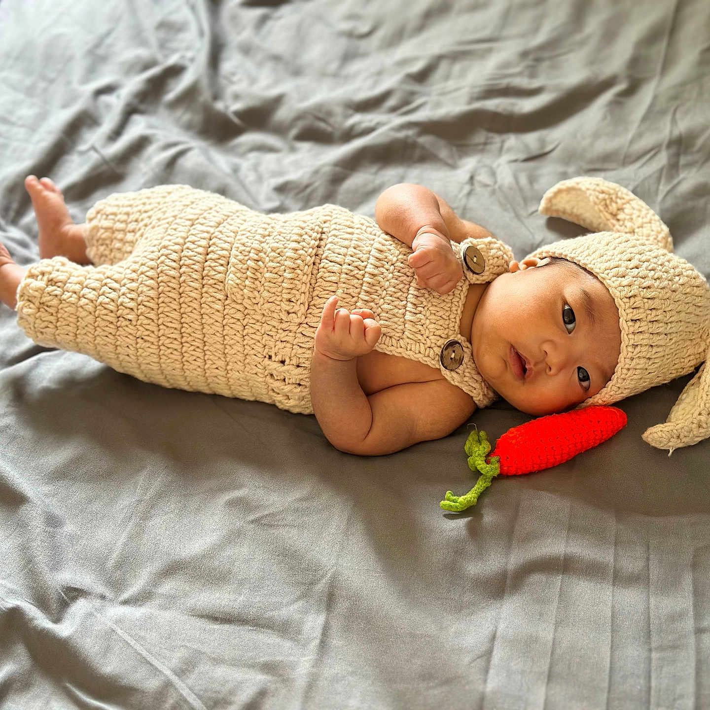 Dior Hendrix is registered to the contest to win money with this photo: adorable, baby, bed, bunny_ears, carrot_toy, child, cozy, cute, face, gray_bedspread, handmade, headwear, indoor, infant, knitted_outfit, lying_down, newborn, portrait, soft_texture, toy