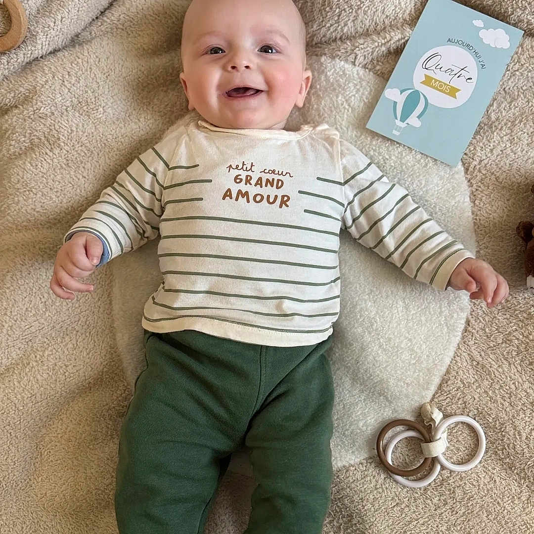 Naël participe au concours pour gagner de l'argent avec cette photo : baby, baby_toys, blanket, child, cozy, cute, face, feet, green_pants, hands, happy, head, indoors, infant, lying_down, milestone_card, playful, smiling, soft_texture, striped_shirt