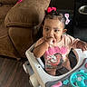 Leilani joined the competition — help win amazing prizes! toddler, child, baby_walker, indoor, brown_couch, wooden_floor, pink_bow, hair_bow, moana_shirt, cute, curious, sitting, playful, infant, person, toy, hand_in_mouth, young_child, bright_eyes, home