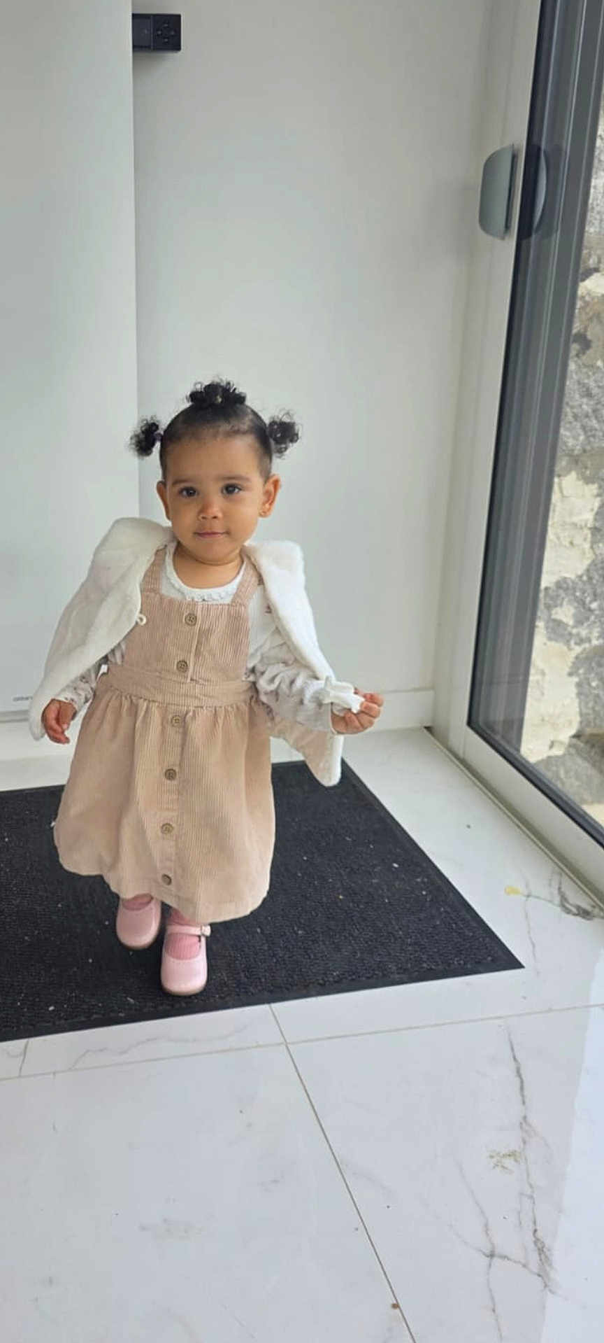 éloïse a rejoint le concours — aidez-le/la à gagner de superbes lots ! toddler, child, girl, indoor, dress, pink_shoes, jacket, pigtails, black_mat, glass_door, floor_tiles, window, white_wall, buttons, standing, cute, young_child, portrait, floor, smiling