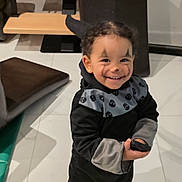 éloïse participe au concours pour gagner de l'argent avec cette photo : toddler, child, smiling, face_paint, costume, black_clothing, gray_clothing, indoor, floor_tiles, furniture, small_object, curly_hair, earrings, happy, portrait, person, standing, home, cute, playful