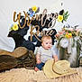 baby, cowhide, flowers, cowboy_hat, saddle, blanket, bucket, feathers, decor, blue_eyes, indoor, person, child, rustic, floral_arrangement, jeans, short_sleeve_shirt, name_sign, soft_texture, cute