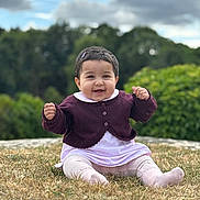 Syra is registered to the contest to win money with this photo: baby, child, smiling, outdoor, grass, purple_cardigan, white_outfit, hair_clip, happy, sitting, nature, greenery, cloudy_sky, cute, portrait, young_child, person, clothing, feet, face