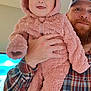 baby, child, man, plaid_shirt, cap, indoor, smiling, holding, pink_bear_suit, fuzzy_clothing, cute, person, portrait, happy, face, hand, cozy, living_room, television, adult