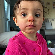Elizabeth is registered to the contest to win money with this photo: toddler, child, face, indoor, pink_sweater, hearts, messy_hair, curious_eyes, portrait, close_up, living_room, couch, pillow, person, cute, expression, young_child, clothing, sitting, real_life