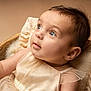 adorable, baby, blue_eyes, child, close_up, cream_dress, cute, expression, face, indoors, infant, looking_up, newborn, portrait, ruffled_cushion, skin, soft_lighting, soft_texture, toddler, warm_colors