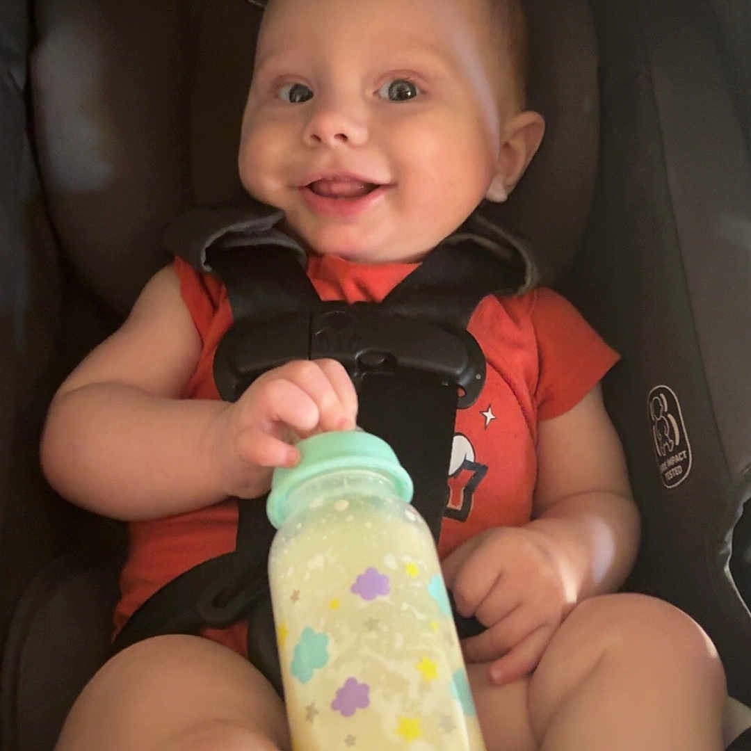 Kalix joined the competition — help win amazing prizes! baby, baby_bottle, bottle, car_seat, child, cute, face, feeding, happy, holding, indoors, infant, milk, orange_shirt, person, portrait, seatbelt, sitting, smiling, young_child