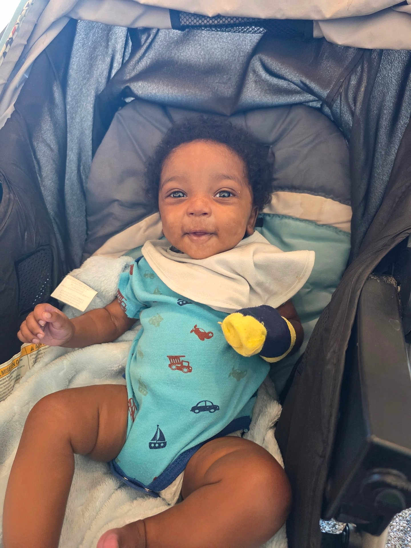 Andrea is registered to the contest to win money with this photo: baby, child, stroller, onesie, bib, blanket, mittens, smiling, infant, cute, happy, portrait, seated, indoors, cozy, clothing, person, face, human, baby_toy
