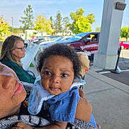 Andrea is registered to the contest to win money with this photo: baby, infant, child, person, adult, outdoor, daylight, car, woman, glasses, clothing, holding, curious, face, portrait, bench, trees, pavement, hand, sleeve