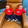 baby, twins, red_hoodie, navy_pants, black_shoes, smiling, chair, leather_chair, indoor, carpet, wall_outlet, happy, cute, sitting, child, person, two_children, casual_clothing, home, playful