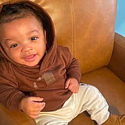 Kevin And Keldrick is registered to the contest to win money with this photo: toddler, child, smiling, hoodie, brown_clothing, cream_pants, boots, leather_chair, indoor, happy, cute, person, seated, baby, face, young_child, casual_clothing, relaxed, portrait, cozy