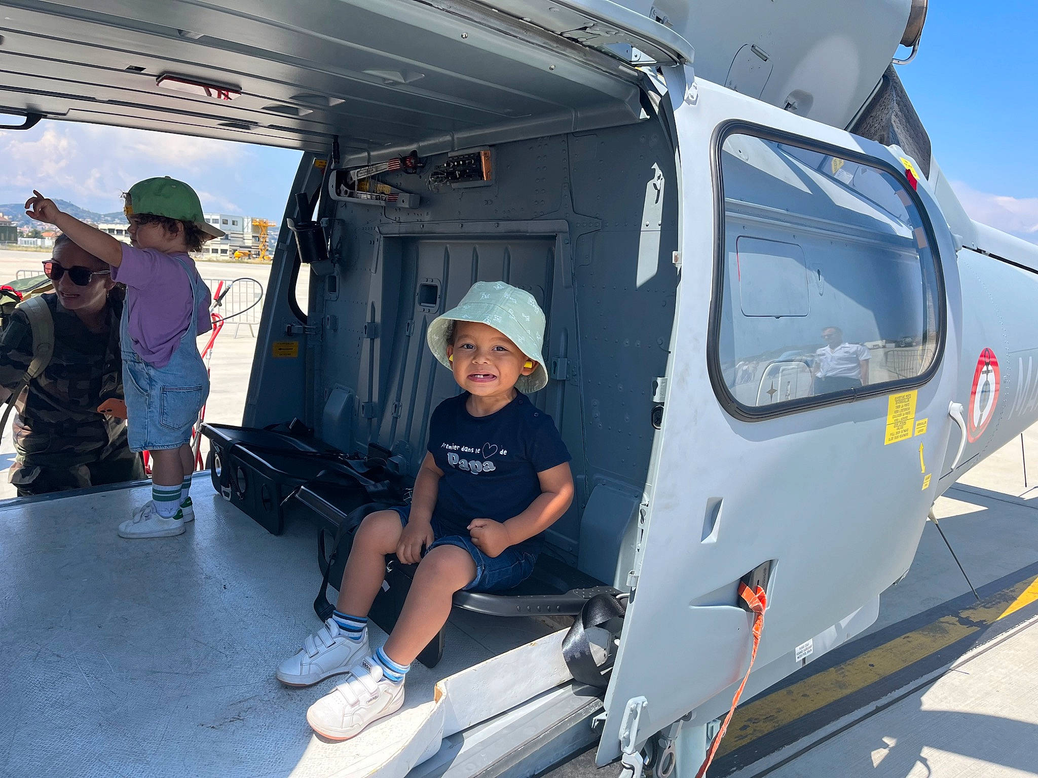 Armand a rejoint le concours — aidez-le/la à gagner de superbes lots ! aerospace_engineering, aerospace_manufacturer, aircraft, automotive_exterior, aviation, baseball_cap, engineering, hat, headwear, helicopter, joy, mode_of_transport, motor_vehicle, person, recreation, rotorcraft, shorts, sky, smile, sun_hat