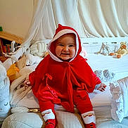 Lara a rejoint le concours — aidez-le/la à gagner de superbes lots ! baby, bed, blanket, child, christmas, cozy, cute, face, happy, holiday, hood, indoors, person, pillow, plush_toy, red_clothing, santa_outfit, smiling, sock, stuffed_animal