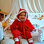 baby, bed, blanket, child, christmas, cozy, cute, face, happy, holiday, hood, indoors, person, pillow, plush_toy, red_clothing, santa_outfit, smiling, sock, stuffed_animal
