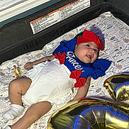 Eliana is registered to the contest to win money with this photo: baby, infant, child, smiling, lying_down, portrait, patriotic, blue_outfit, red_bow, white_dress, headband, pacifier, socks, play_mat, floral_pattern, balloons, birthday, indoor, nursery, celebration