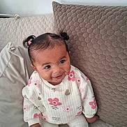 Ava a rejoint le concours — aidez-le/la à gagner de superbes lots ! baby, child, smiling, pigtails, couch, cushion, patterned, white_clothing, pink_flowers, golden_hearts, sitting, indoors, happy, cute, portrait, young_child, infant, cozy, homedecor, person