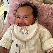 Ava participe au concours pour gagner de l'argent avec cette photo : baby, child, infant, smiling, bib, knit_sweater, button, curly_hair, pillow, blanket, drool, hand, eyes, cheeks, indoors, portrait, cozy, seat, patterned_clothing, cute