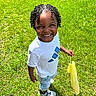 Nycere is registered to the contest to win money with this photo: child, smiling, outdoor, grass, lawn, sunny, portrait, standing, curly_hair, braids, white_shirt, shorts, sneakers, yellow_bag, plastic_bag, playful, happy, front_view, storm_drain, photography