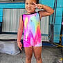 child, girl, standing, peace_sign, colorful_clothing, rainbow, outdoor, concrete, swing, footwear, sandals, smiling, shorts, tank_top, curly_hair, playful, portrait, daylight, background, furniture