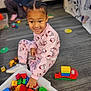 child, toddler, indoor, play, toys, building_blocks, hello_kitty, pajamas, smiling, floor, carpet, person, fun, colorful, plastic_blocks, young_child, sitting, hair, casual_clothing, playroom