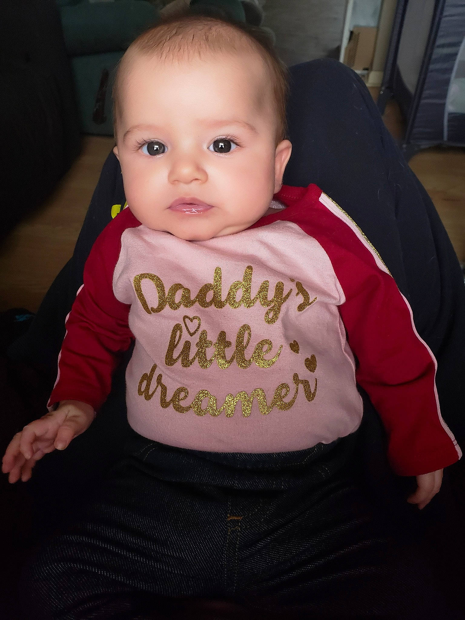 Kailey is registered to the contest to win money with this photo: baby, baby_products, baby_toddler_clothing, cheek, child, eye, face, head, iris, lip, outerwear, person, product, sitting, skin, sleeve, smile, t_shirt, toddler