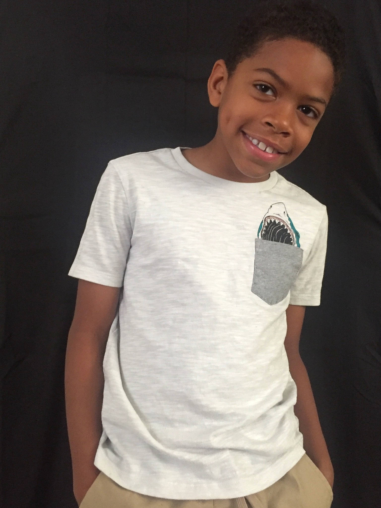 Jeremiah is registered to the contest to win money with this photo: arm, child, clothing, cool, ear, joy, neck, person, photography, pocket, shoulder, sleeve, smile, sportswear, t_shirt, top, white