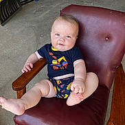 Bodhi is registered to the contest to win money with this photo: baby, child, infant, sitting, chair, maroon, leather, clothing, blue_eyes, playful, indoor, concrete_floor, tool, wooden_armrest, cute, smile, person, shorts, tshirt, casual