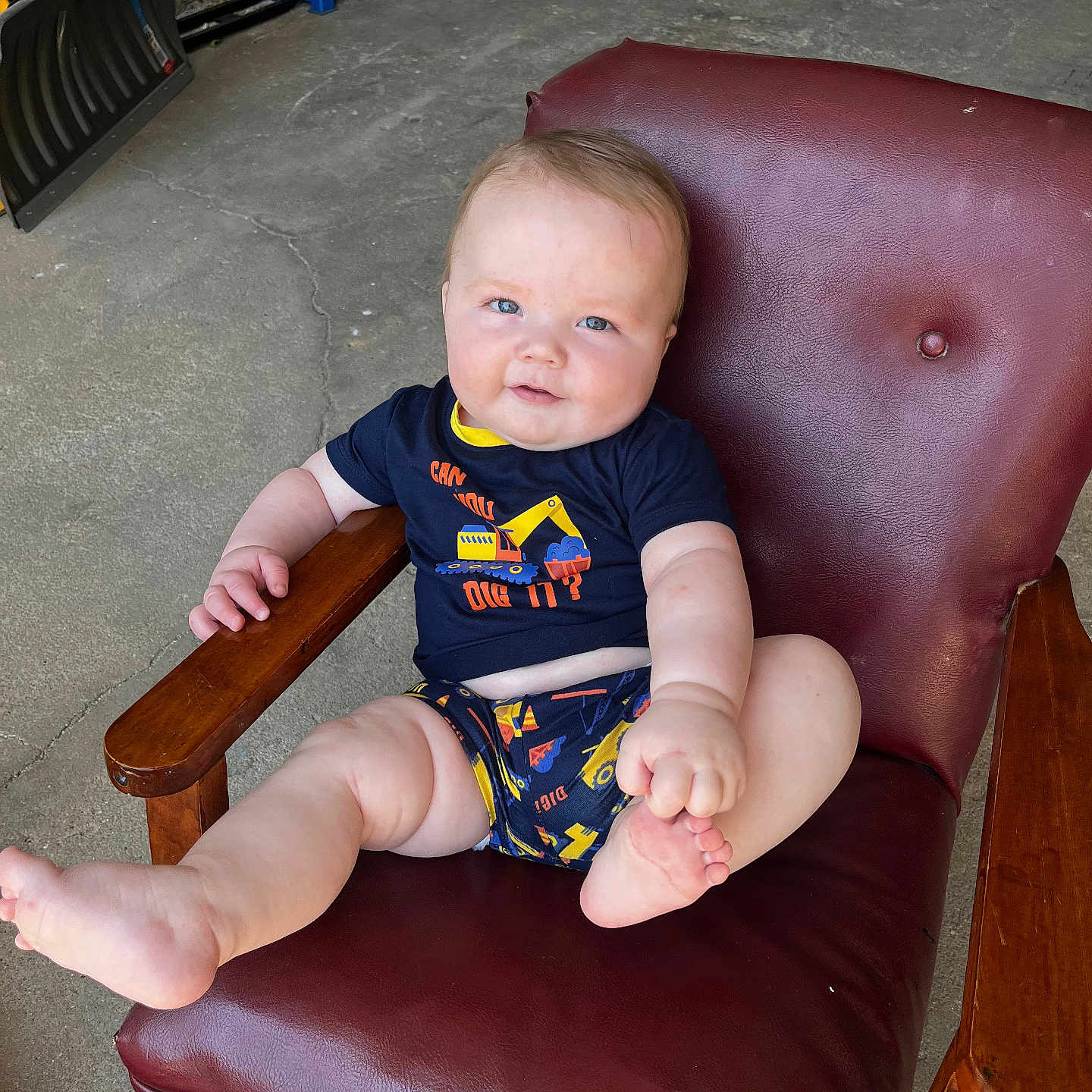 Bodhi is registered to the contest to win money with this photo: baby, child, infant, sitting, chair, maroon, leather, clothing, blue_eyes, playful, indoor, concrete_floor, tool, wooden_armrest, cute, smile, person, shorts, tshirt, casual