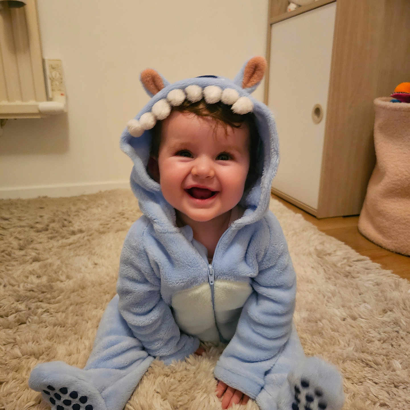 Giulia participe au concours pour gagner de l'argent avec cette photo : baby, blue_onesie, carpet, child, clothing, costume, cute, ears, floor, furniture, happy, indoor, infant, monster_costume, person, portrait, room, sitting, smiling, teeth