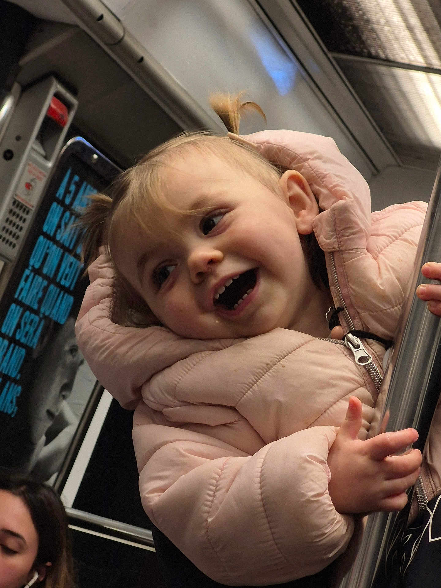 Layana participe au concours pour gagner de l'argent avec cette photo : child, toddler, pigtails, pink_coat, winter_jacket, smile, laughing, subway, metro, public_transport, pole, hand, face, portrait, candid, indoor, advertisement, zipper, passenger, crumbs