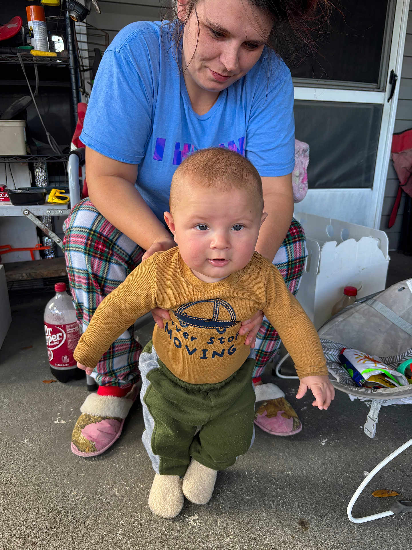 Jayce joined the competition — help win amazing prizes! baby, adult, woman, porch, slippers, plaid_pajamas, sweatshirt, holding, hands, dr_pepper_bottle, concrete_floor, screen_door, door, toy_bag, candid, expression, cozy, indoor_outdoor, portrait, supporting_hands