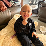 Everest is registered to the contest to win money with this photo: toddler, child, smile, black_clothing, nike, sitting, indoor, couch, plush_toy, carpet, hand, face, happy, cozy, home, furniture, curious, light, portrait, casual