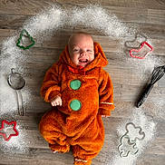 August is registered to the contest to win money with this photo: baby, child, cookie_cutters, costume, cute, festive, floor, flour, gingerbread_costume, green_buttons, happy, holiday, indoors, infant, playful, red_bow, sieve, smiling, whisk, wooden_floor