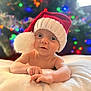 baby, infant, santa_hat, holiday, christmas_lights, blanket, face, smiling, cute, indoors, soft_texture, festive, child, portrait, holiday_season, warm_lighting, celebration, christmas_tree, holiday_mood, young_child
