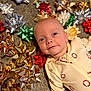 baby, infant, smile, face, carpet, gift_bows, red, green, gold, silver, holiday, cute, lying_down, onesie, pattern, blue_eyes, indoors, closeup, festive, child