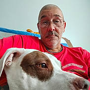 Leah is registered to the contest to win money with this photo: animal, blanket, brown_patch, casual, chain_necklace, closeup, couch, dog, face, glasses, head, home, indoor, man, pet, portrait, red_shirt, relaxed, selfie, white_dog