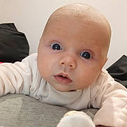 Malakai is registered to the contest to win money with this photo: baby, infant, face, wide_eyes, curious, sweater, white_clothing, close_up, indoor, cushion, soft_fabric, person, child, cute, skin, head, hand, expression, portrait, home