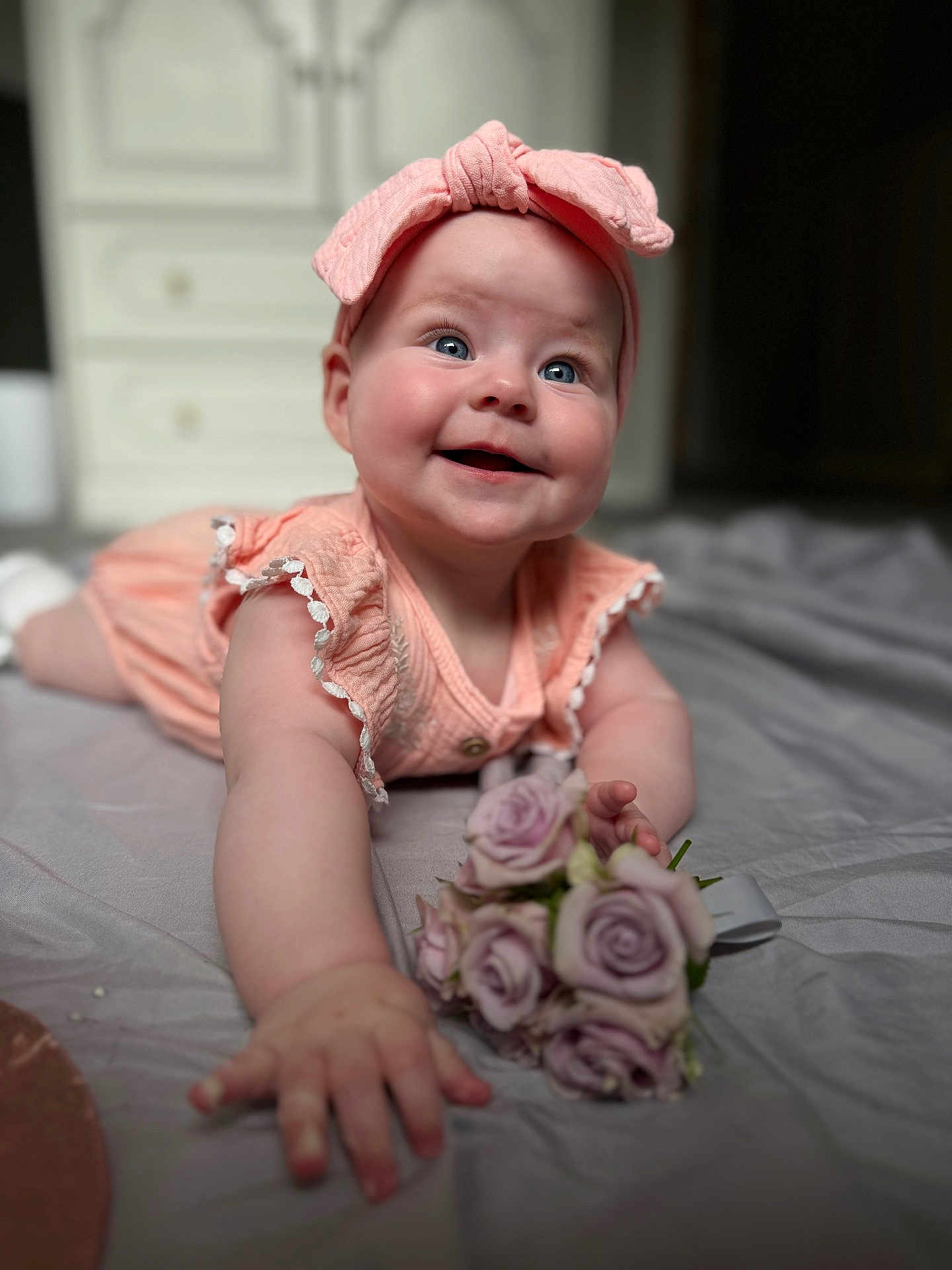 Leah is registered to the contest to win money with this photo: baby, child, smiling, pink_headband, pink_dress, flowers, roses, indoor, portrait, closeup, crawling, happy, cute, infant, hands, face, blue_eyes, soft_light, blanket, home