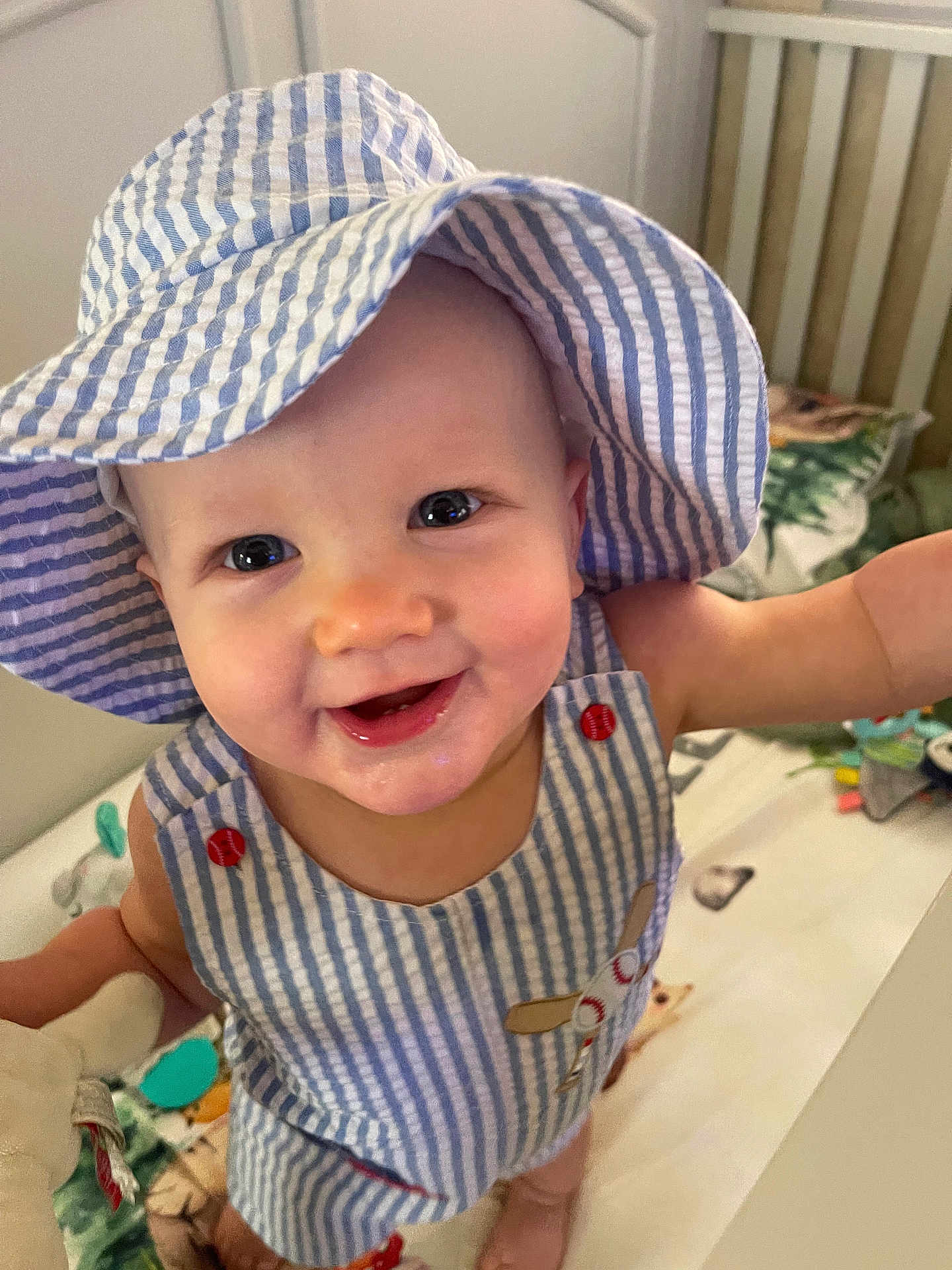 Brantley is registered to the contest to win money with this photo: baby, child, smiling, hat, striped_clothing, crib, toy, indoor, face, happy, cute, infant, closeup, apparel, person, playful, cheerful, blue, white, young