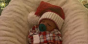 Brantley is registered to the contest to win money with this photo: baby, infant, pacifier, santa_hat, plaid_pajamas, christmas_tree, ornaments, lights, cushion, blanket, holiday, festive, cozy, sleeping, indoor, decorations, celebration, warm_lighting, cute, child