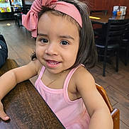 Lily joined the competition — help win amazing prizes! child, toddler, girl, smiling, pink_bow, headband, pink_dress, table, wooden_table, indoor, restaurant, chair, brown_floor, happy, portrait, person, cute, young_child, casual_clothing, seated
