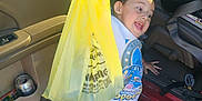 Dean joined the competition — help win amazing prizes! child, toddler, yellow_bag, car_door, parking_lot, shorts, tshirt, sandals, smiling, happy, standing, outdoor, daylight, plastic_bag, toy_car_graphic, concrete, seatbelt, vehicle, hand, excited