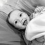 Athena is registered to the contest to win money with this photo: baby, smiling, blanket, face, infant, happy, lying_down, cushion, cozy, black_and_white, child, portrait, cute, soft_texture, indoors, clothing, person, closeup, expression, comfort