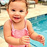 baby, toddler, child, smiling, happy, poolside, swimming_pool, outdoor, sunny, portrait, curly_hair, pink_swimsuit, standing, arms, hands, tropical_plants, patio, lounge_chair, water, family_photo