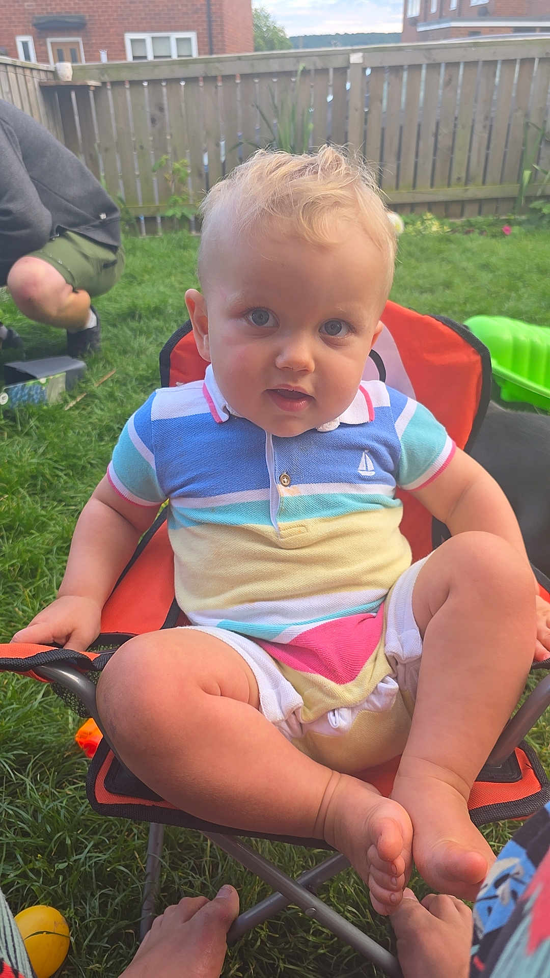 Blake is registered to the contest to win money with this photo: child, toddler, outdoor, grass, chair, colorful_clothing, blue_eyes, shorts, polo_shirt, fence, person, toy, barefoot, summer, garden, cute, sitting, playful, baby, daylight