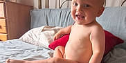 Blake joined the competition — help win amazing prizes! toddler, child, smiling, bed, blanket, pillow, blue_blanket, red_pillow, metal_headboard, wooden_dresser, framed_photo, indoor, happy, skin, person, furniture, room, portrait, sitting, cute