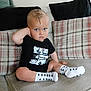 Blake is registered to the contest to win money with this photo: toddler, child, blue_eyes, black_tshirt, car_graphic, white_socks, stars, plaid_cushions, couch, indoor, seated, cute, portrait, young_child, casual_clothing, comfort, home, furniture, expression, pose