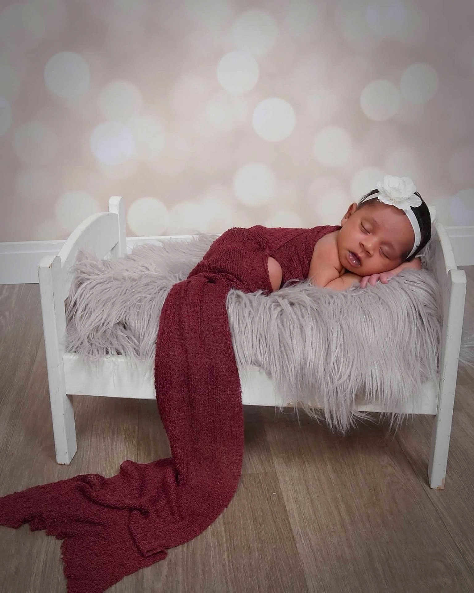 Annalee joined the competition — help win amazing prizes! baby, sleeping, bed, blanket, headband, flower, maroon_cloth, fur_texture, wood_floor, white_bed, infant, cozy, portrait, indoor, cute, peaceful, resting, child, soft_light, decor